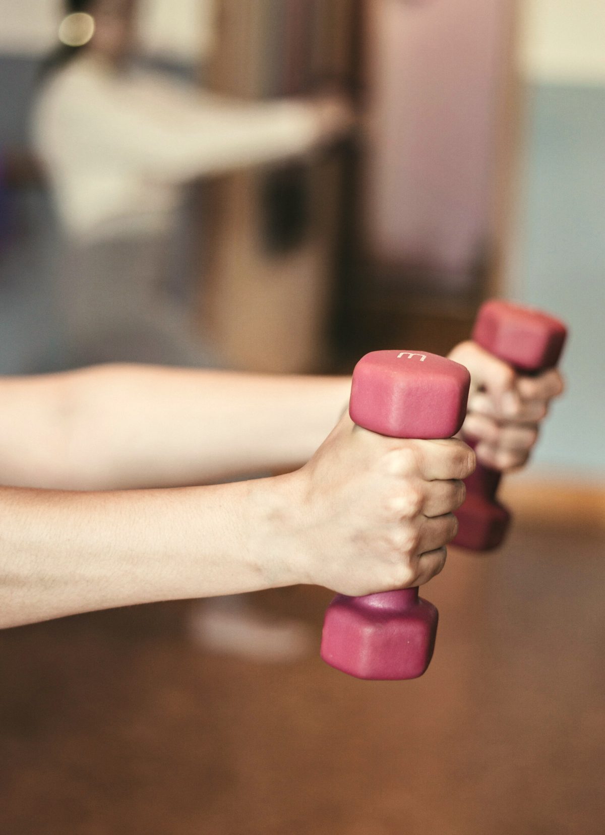 Two hands holding light pink dumbbells at shoulder height